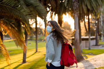 Young woman outdoor wearing face mask, social distancing isolated from other people wearing face...