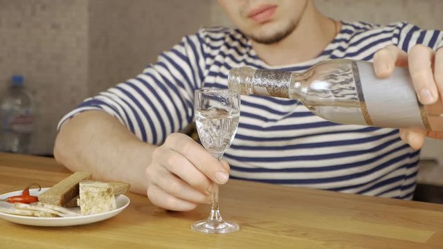 a young Russian man dressed in a vest pours vodka from a bottle into a glass. alcoholic drink