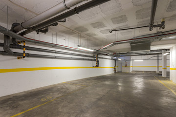Common garage for parking cars in a multi-storey building with sewer pipes.