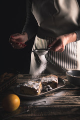 Close up of female chefs hands servicing slice of cake with cherries, sprinkling powdered sugar.