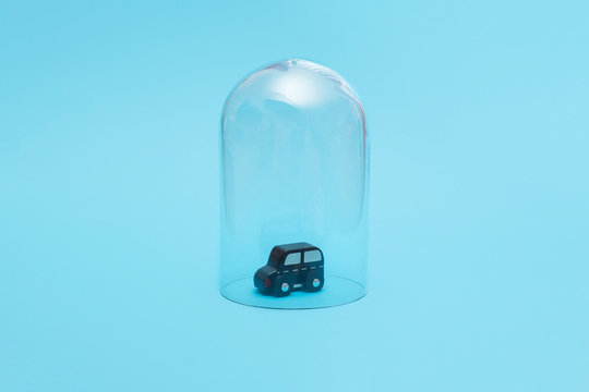 Kids black wooden toy car in quarantine under a glass cloche dome on a blue background with copy space and room for text