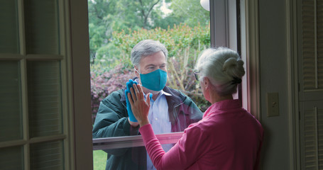 A mature man lovingly checks on an elderly relative but follows the social distancing mandate...