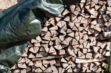 woodpile with chopped fuel wood covered with a tarpaulin