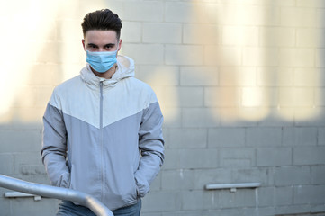 Portrait of a Caucasian young man in a medical mask outdoors in the city on a gray background on a...