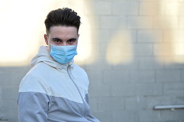 Portrait of a Caucasian young man in a medical mask outdoors in the city on a gray background on a...