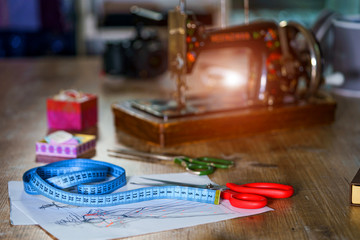 Blue measuring tape and scissors with red handle on sketches with dresses. Tailor`s sketches,...