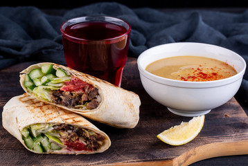 Meat rolls in lavash with fresh vegetables with a plaid of soup, which is served with a slice of lemon and a glass of compote
