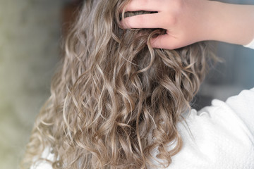 teenage girl with natural wavy hair. blond girl touching her hair, back view. natural curly no brush method for beautiful stylish look.