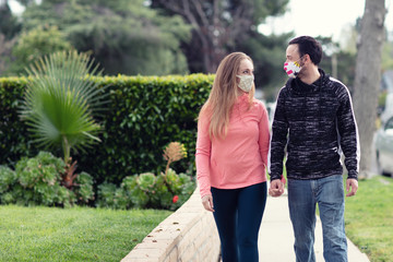 Fototapeta premium A young couple walking in the neighborhood wearing fabric face masks. Covering face in public is recommended by CDC in many countries during to Covid-19 coronavirus pandemic.