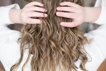 teenage girl with natural wavy hair. blond girl touching her hair, back view. natural curly no brush method for beautiful stylish look. trendy messy style.