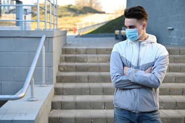Fototapeta premium Photo Caucasian young man in a medical mask in a light jacket outdoors on a city background on a sunny day