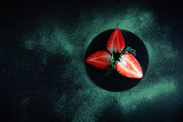 Top view of red strawberries in a black circle on the table with spilled matcha around