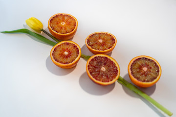 Slices of blood orange with a tulip on a white table 