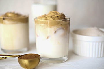 Iced frothy Dalgona Coffee, trendy fluffy creamy whipped coffee. Korean drink latte espresso with coffee foam in glass. made of instant coffee, sugar, hot water and milk. milk bottle, sugar and cups.