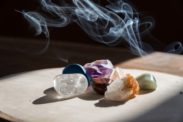 Mineral stones on the wooden plate with smoke in the background during beautiful morning light indoor. Cleansing and purifying the energy and vibe indoor. Part of meditation, therapy, aromatherapy. 