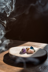 Mineral stones on the wooden plate with smoke from burning palo santo wood stick. 