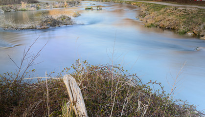 A river flows quietly and slowly in the winter between dry grass and stones as a long-term shot