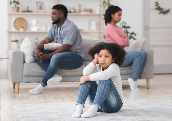 Upset little black girl sitting separately from parents after their argue