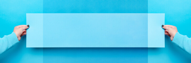 Obraz premium piece of paper in the female hand over blue trendy background, empty blank for advertisement