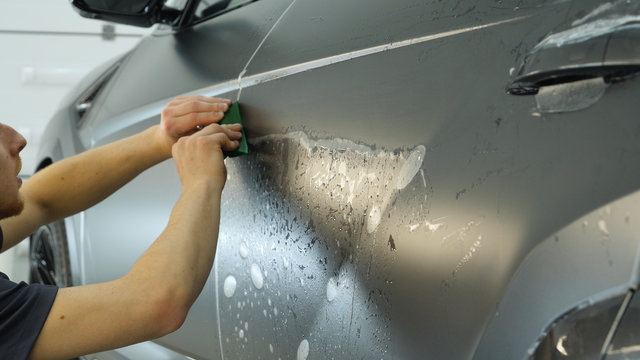 Close up of paint protection film installation on modern luxury car. PPF is polyurethane film that wrap car paint to protect paint surface from stone chips, bug splatter, and abrasion.