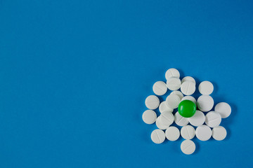 heap of white pills and one green, on a blue background