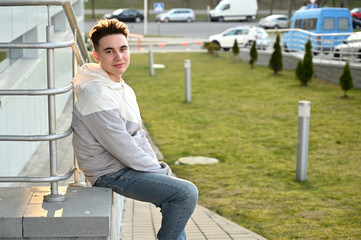 Obraz premium Portrait of a Caucasian young brunette man in a light jacket outdoors on a city-background. A model stands next to the railing of the stairs
