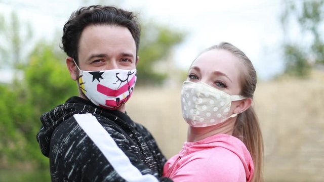 A young beautiful couple embracing each other in a tight hug with their face covered in a cloth face mask. Covering the face is recommended in many countries during to coronavirus outbreak.