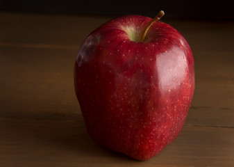 still life photography, low key light or dark food, red apple on a wooden table, macro photography or close up.