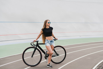 Cycling and fitness. Young beautiful fit woman with perfect body in sportswear with the bike outdoors on the track. Sportive and healthy lifestyle, cyclist working out, training, fashion, beauty.