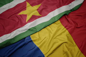 waving colorful flag of romania and national flag of suriname.