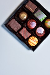 Set of delicious chocolate candy in black elegant box with selective focus on neutral background. Gift box with various chocolate truffles and bonbons. set of exclusive handmade candies. Vertical 