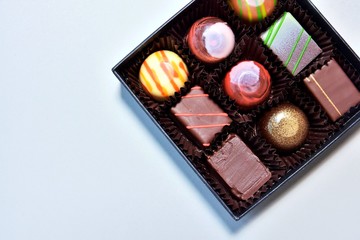 Set of delicious chocolate candy in black elegant box with selective focus on neutral background. Gift box with various chocolate truffles and bonbons. set of exclusive handmade candies.