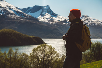 Young man with a backpack standing on the background of mountains and lake. Space for your text message or promotional content. Travel lifestyle concept