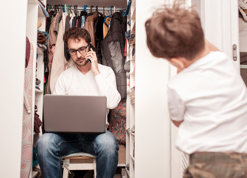 Busy father trying to find a quiet place in a wardrobe between clothes  to hide from children for a work at the laptop. Work from home. Home office. Quarantine. Freelancer.