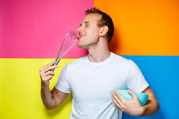 young guy man in a white T-shirt, colorful background, kitchen utensils, cook, emotions photo