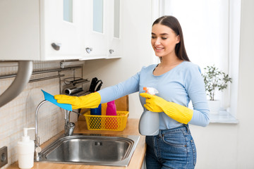 Smiling woman cleaning kitchen furniture using spray