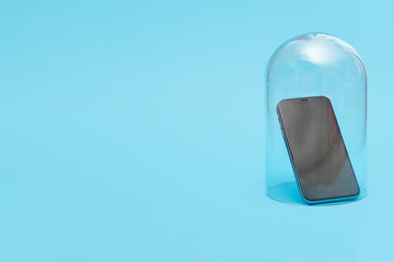 Mobile smartphone in quarantine under a glass cloche dome on a blue background with copy space and room for text with a right side composition