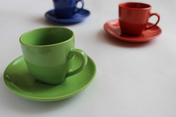 a blue or green Cup a mug with a saucer stands on the table on a white background behind you can see two more mugs red and blue or green morning Breakfast tea or coffee