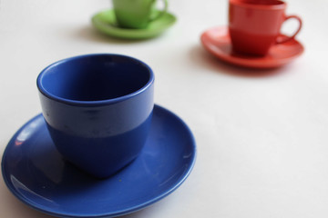 a blue or green Cup a mug with a saucer stands on the table on a white background behind you can see two more mugs red and blue or green morning Breakfast tea or coffee