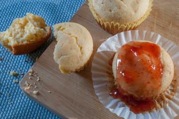 Cornmeal cupcakes with strawberry jam on top on a cutting board and blue surface, cupcake crumbles