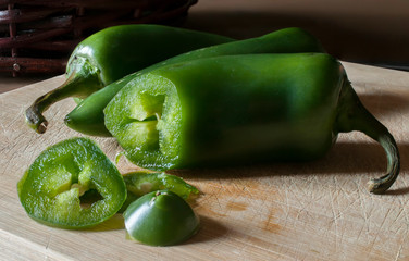 Chile jalapeño slices on a cutting board and a basket of chiles in the background