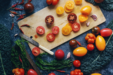 Mix of colorful raw fresh tomatoes and herbs on dark stone table and old wooden board