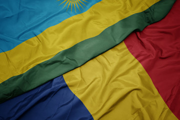 waving colorful flag of romania and national flag of rwanda.