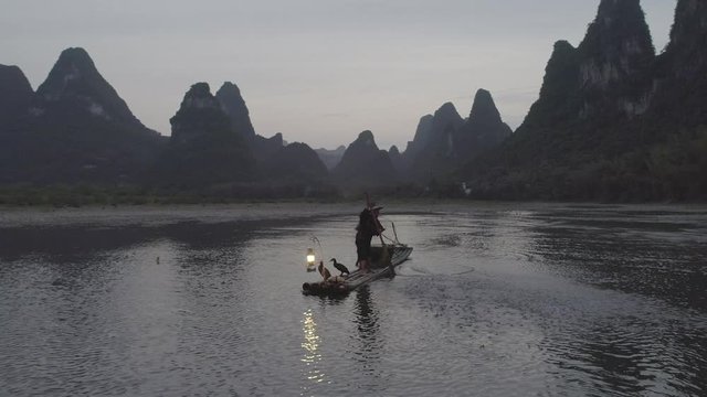 Slow moving  panning arial shot of Chinese cormorant fisherman punting a bamboo raft across a broad expanse of water with karst towers in the background