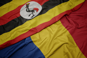 waving colorful flag of romania and national flag of uganda.