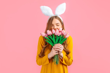 happy Easter. Happy woman in Easter Bunny ears, girl with a bouquet of tulips, on an isolated pink background