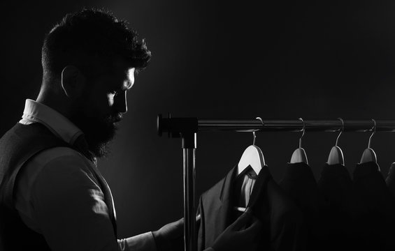 Man in suit. Shirts and suits in a male luxury store. Row of man suit jackets on hangers. Tailor in his workshop, designer. Bearded man in suit. Client is elegant guy, classic suits and jackets.