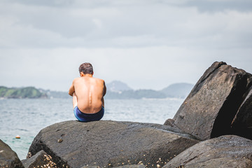 a man sits on a stone by the sea and waits for something