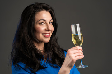 Attractive latin mature woman smiling and holding glass of champagne or wine on grey studio background. Drinking alcohol concept