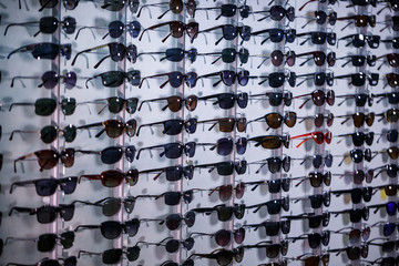 Fototapeta premium A row of glasses to protect from the sun. Store points. Stand with sunglasses in the optics store. Female hand shows glasses. Presentation of points. Close-up